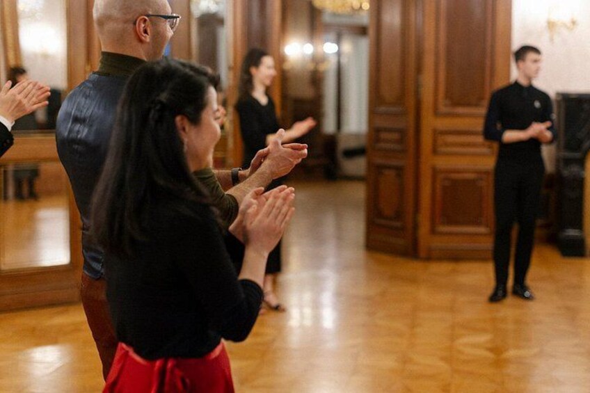 A group of people clapping in a room with wooden floors and paneled walls. 4