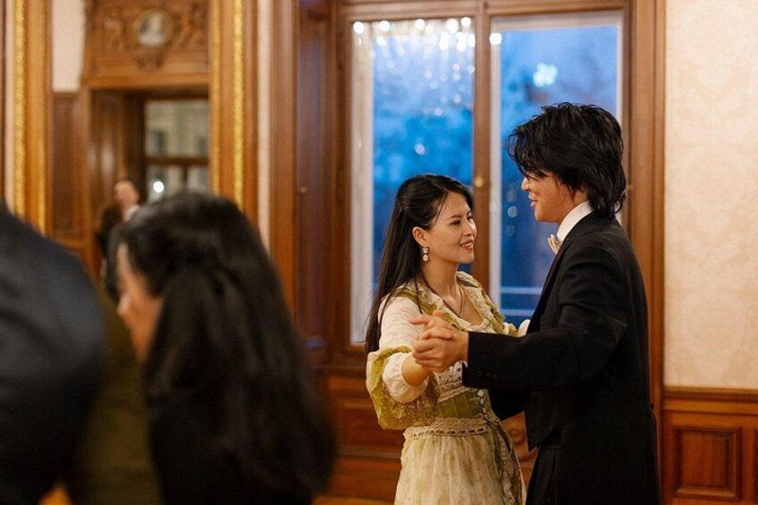 A man and a woman dancing in a ballroom with wooden paneling and a large window. 5