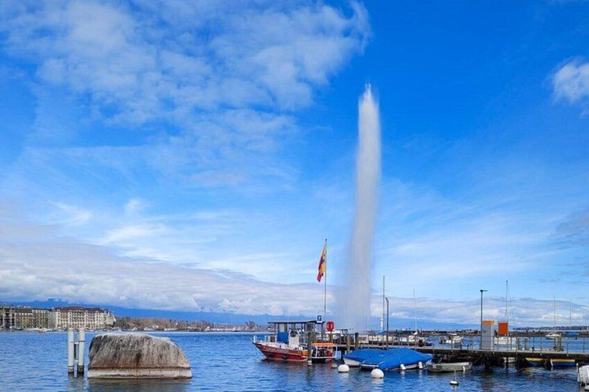 A water fountain, boats, and a distant cityscape under a clear sky. 4