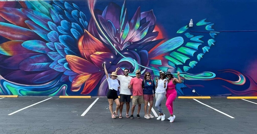 A group of people posing in front of a colorful mural with a parking lot in the foreground. 3