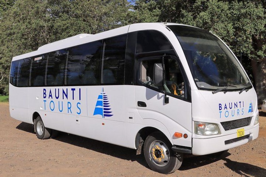 En hvid bus med 'BAUNTI TOURS' skilte langs en grusvej. 2