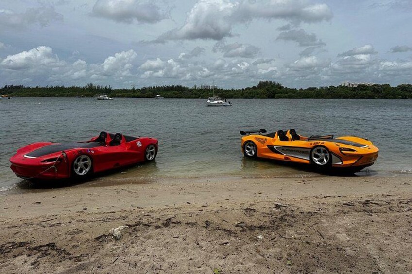 Two sports cars parked on a beach with a lake and a boat in the background. 4