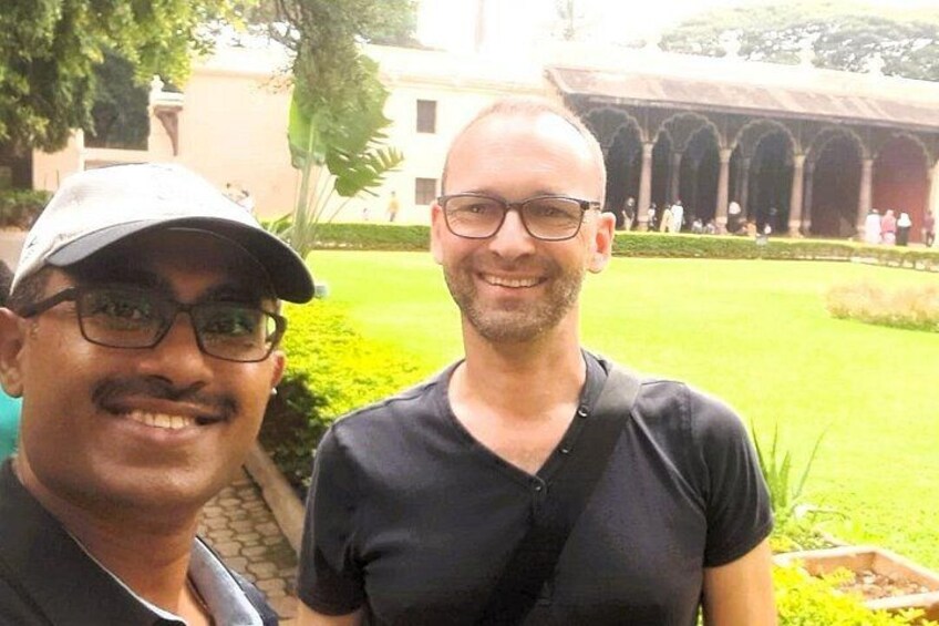 Two men standing outdoors with a building and greenery in the background. 4