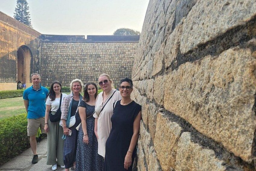 A group of people standing in front of a stone wall with an archway in the background. 3