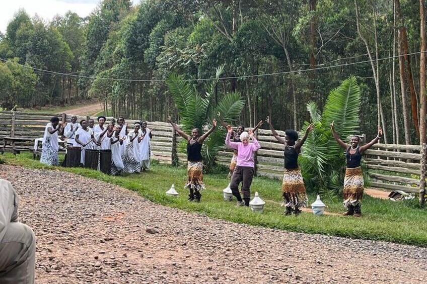 A group of people performing a traditional dance in a rural setting with a dirt path and wooden fence. 5