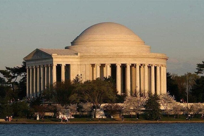 Un gran edificio neoclásico con una cúpula y columnas, rodeado de árboles y una masa de agua. 3