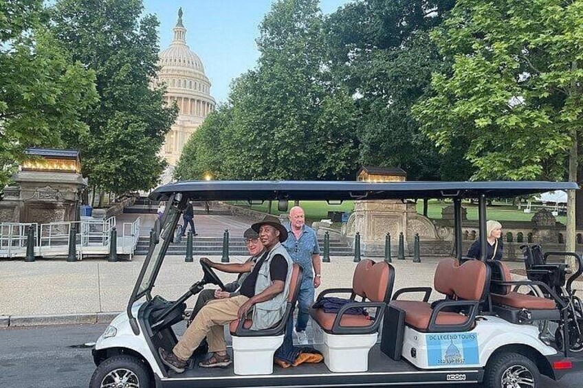 Un carrito de golf con pasajeros, una estatua y el edificio del Capitolio al fondo. 1