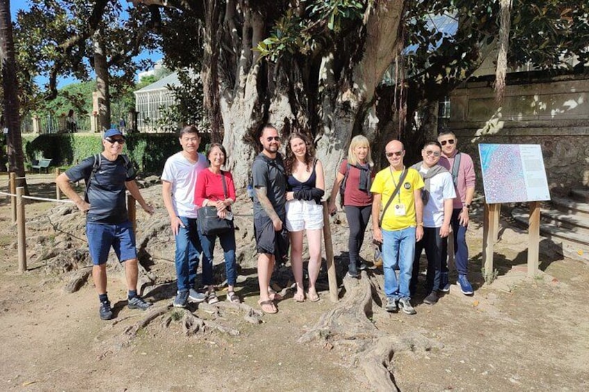 A group of people standing in front of a tree with a signboard. 3