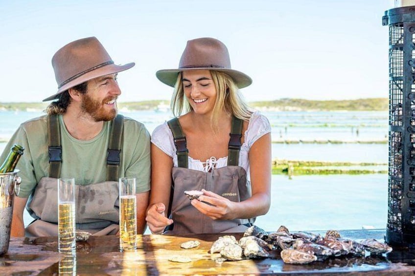 Two people sitting at a table with drinks and oysters. 1