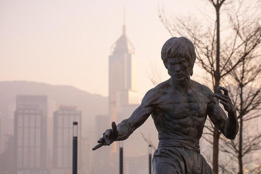 A statue of a muscular figure with outstretched arms, set against a cityscape with modern buildings and a clear sky. 5