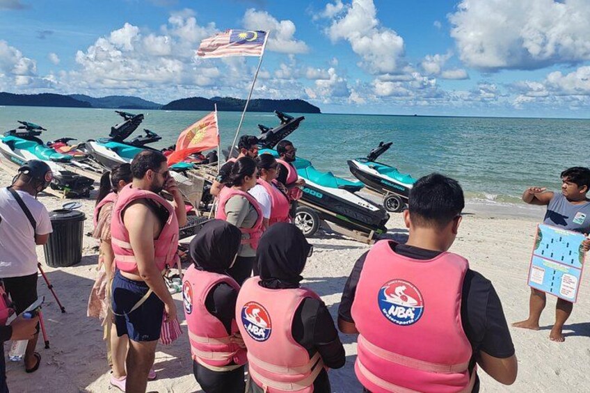 People wearing life jackets and a Malaysian flag on a beach with jet skis. 3