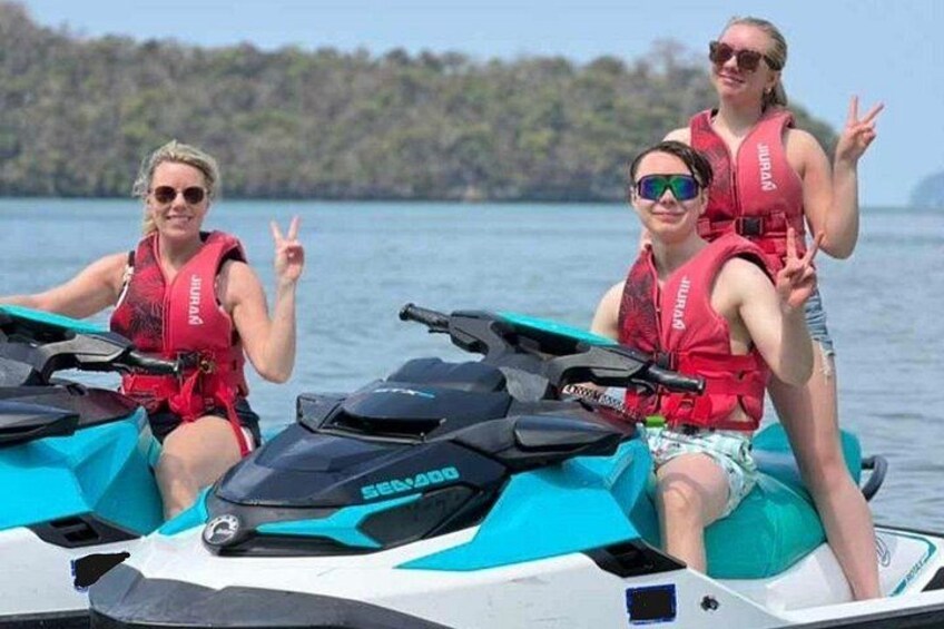 Three people on a jet ski, wearing life jackets, with a lake and trees in the background. 4