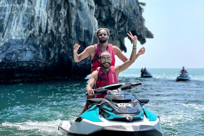A person riding a jet ski on clear water with a rocky cliff in the background. 1