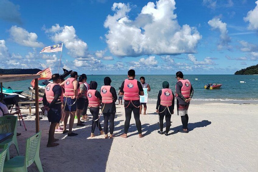 A group of people on a beach with a flag, chairs, and a boat in the water. 2