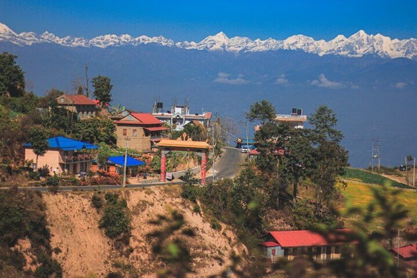 A mountainous village with houses, a road, and a lake with snow-capped peaks in the background. 1