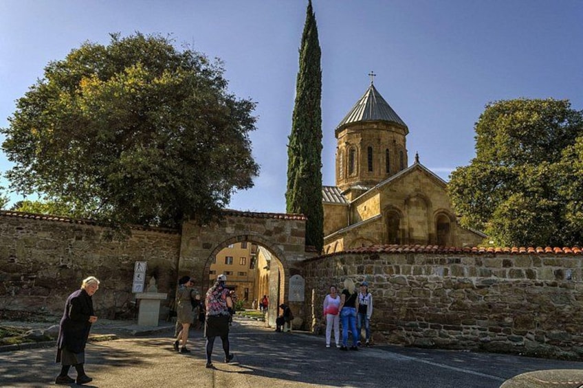 Un mur de pierre ancien, une église surmontée d’un dôme et un grand arbre. 5