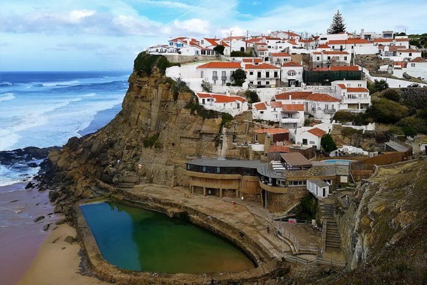 Un village côtier avec des bâtiments blancs, une falaise, une plage et une petite piscine. 1