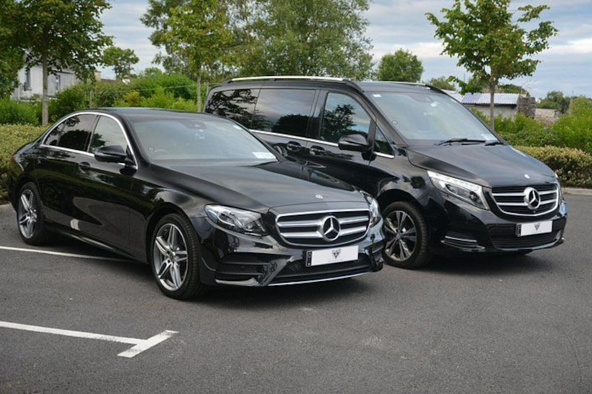 Two black Mercedes-Benz cars parked in a lot with trees and a building in the background. 2