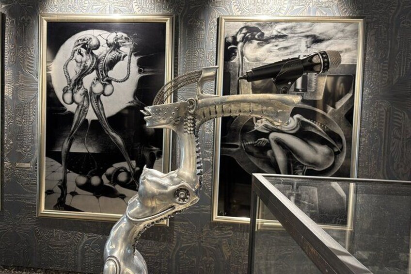 Een sculptuur van een pistool in een galerij, met twee ingelijste kunstwerken aan de muur. 2