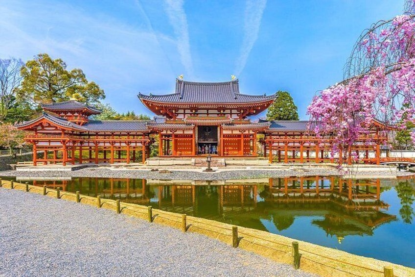 Un edificio japonés tradicional con un estanque en primer plano, rodeado de flores de cerezo. 1