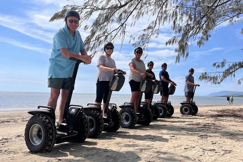 People on Segways on a sandy beach with a clear sky and calm sea in the background. 5