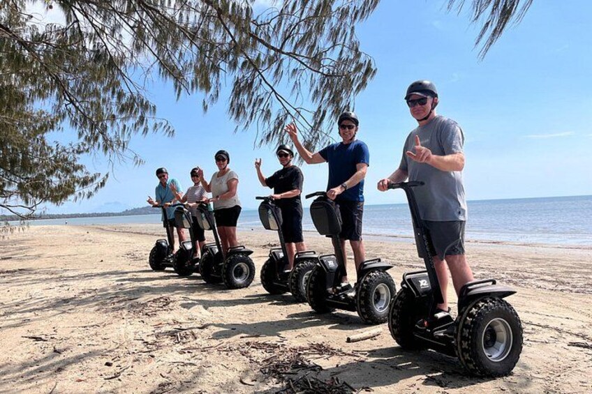 People on segways on a beach with trees and the ocean in the background. 3