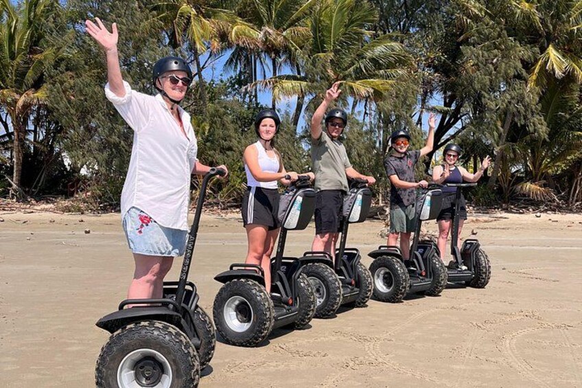 Four people on segways on a sandy beach with palm trees in the background. 2