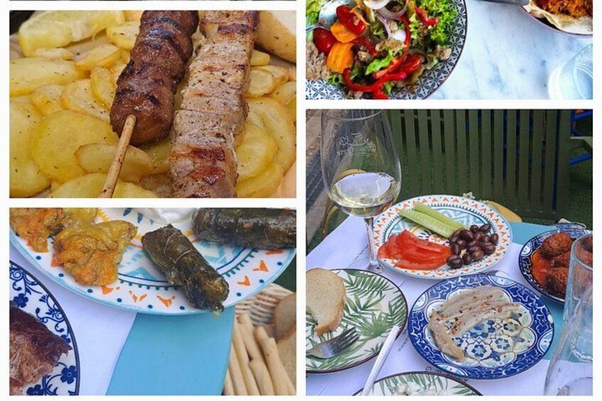 Una mesa con diversos platos, incluyendo carne ensartada, patatas, ensalada, hojas de parra rellenas y pan. 4