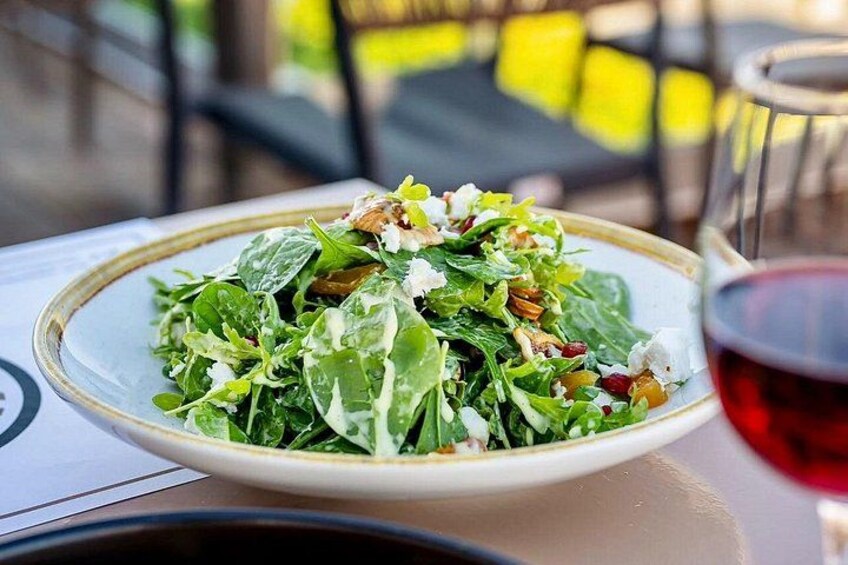 Un plato de ensalada con nueces y queso, una copa de vino tinto y una disposición de mesa. 2