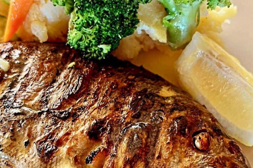 Pescado a la parrilla con marcas de carbón, acompañado de brócoli y rodajas de limón. 4