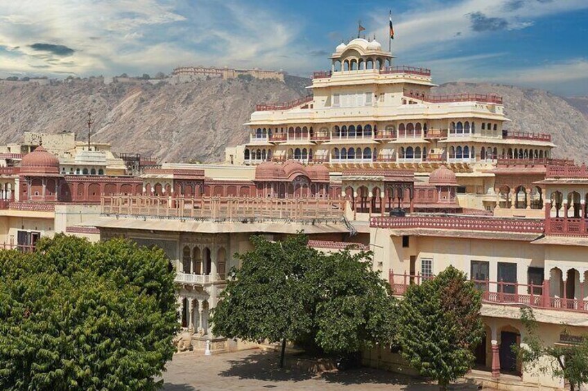 A large, multi-story building with domed structures and arched windows, surrounded by trees and set against a mountainous backdrop. 5