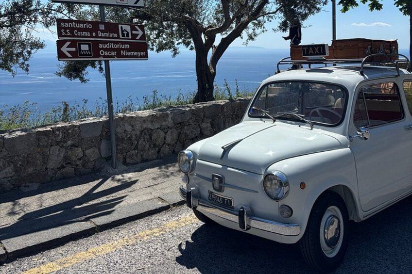 A vintage car parked by a stone wall with a signpost indicating directions to various landmarks. 5