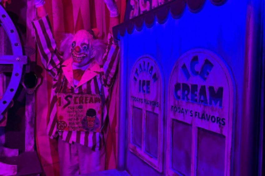 A clown with a sign that reads 'Ice Cream' and 'Today's Flavors' in a brightly lit area with purple lighting. 5