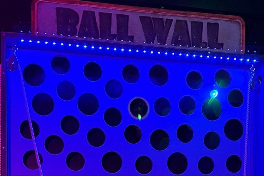 A blue illuminated structure with multiple circular holes and a sign that reads 'BALL WALL'. 2