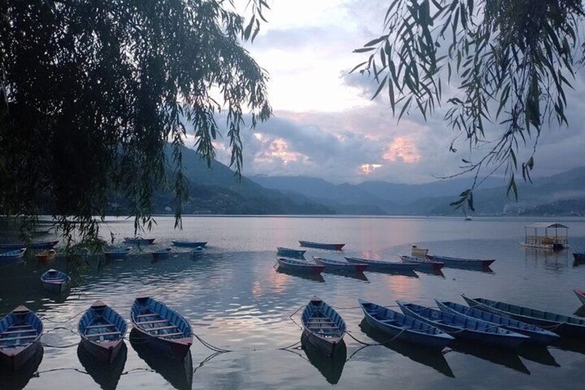 A calm lake with several boats docked along the shore, surrounded by mountains and trees. 3