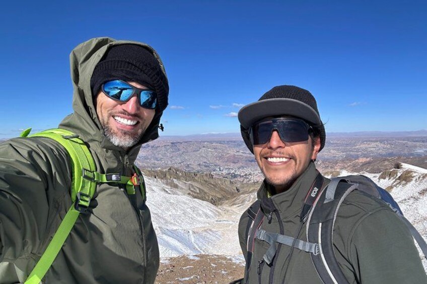 Two people wearing hiking gear, standing on a snowy mountain with a clear sky in the background. 1