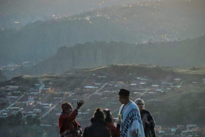 A group of people standing on a hill overlooking a town with buildings and lights in the distance. 3