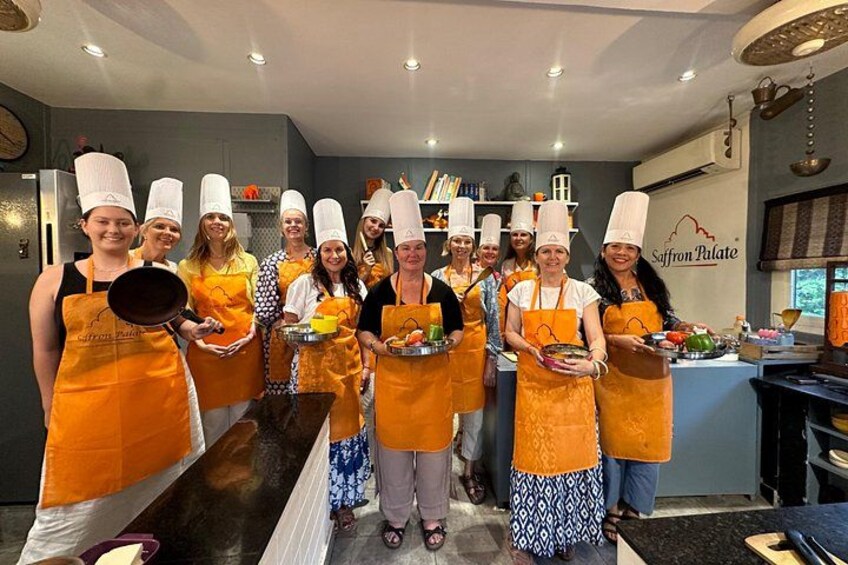 A group of chefs in a kitchen, wearing chef hats and aprons, holding dishes. 1