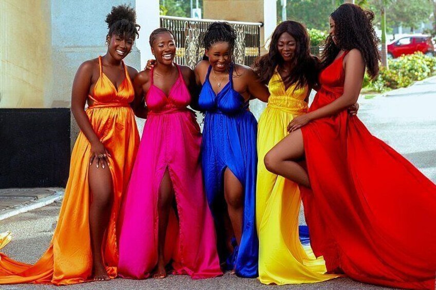 Cinco mujeres con vestidos coloridos de pie en una acera. 5