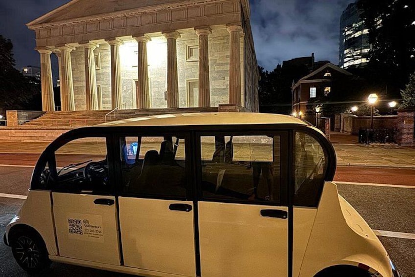 A vintage car parked in front of a classical building with columns. 4