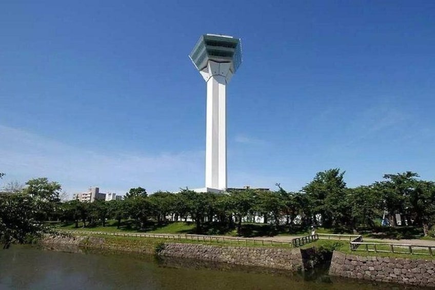 A tall white tower in a park with a pond and trees. 4