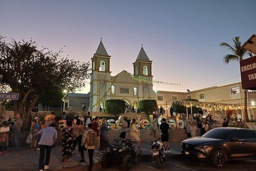 Una calle concurrida con una iglesia, palmeras y una multitud de gente. 2