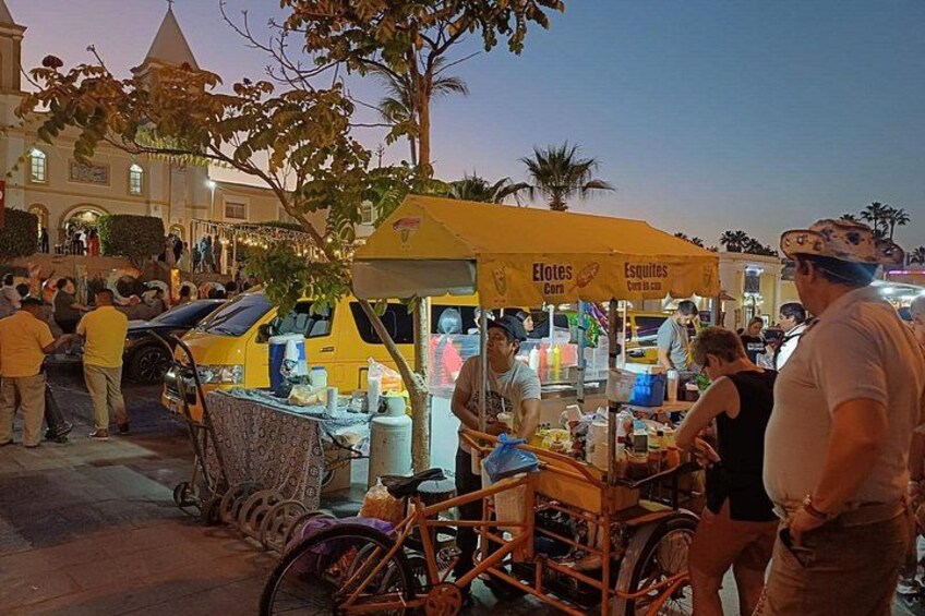A street market with food stalls, a bicycle, and a building in the background. 1