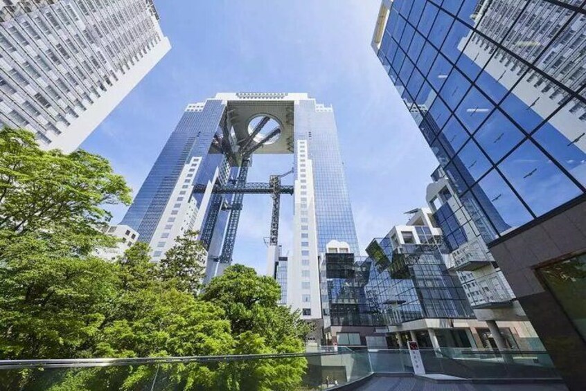 A tall skyscraper with a distinctive central atrium, surrounded by other modern buildings and lush green trees. 1