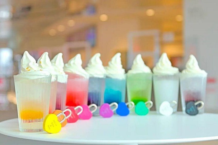 A row of colorful drinks with whipped cream on top, each in a different colored cup. 5