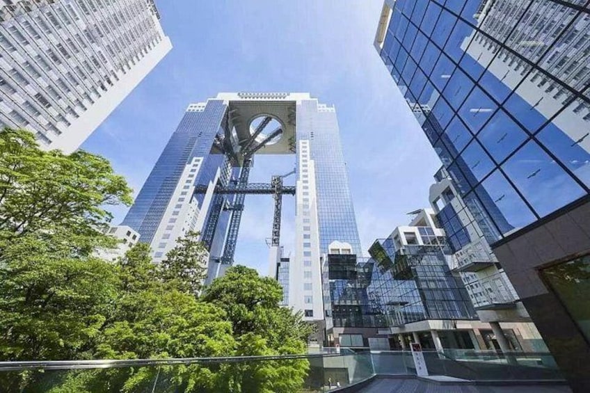 A tall skyscraper with a distinctive central feature, surrounded by modern buildings and trees. 1