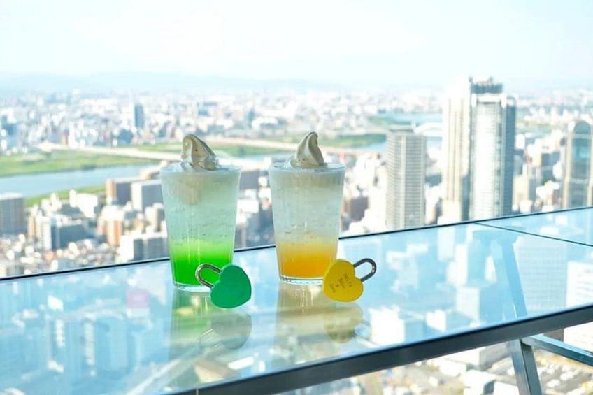 Two drinks on a glass table with a cityscape in the background. 4