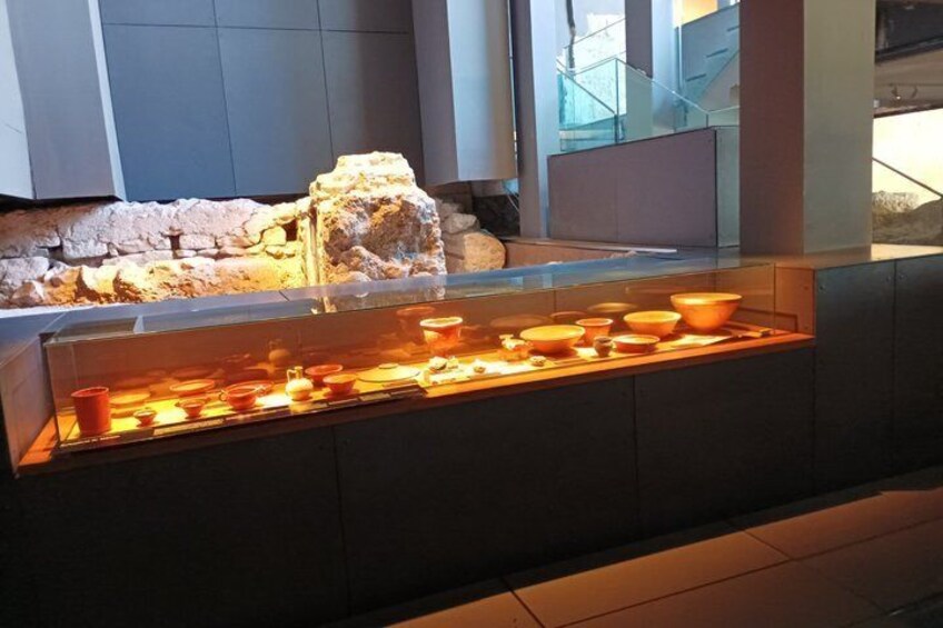 Een museumpresentatie met oude keramiek en een stenen muur op de achtergrond. 4