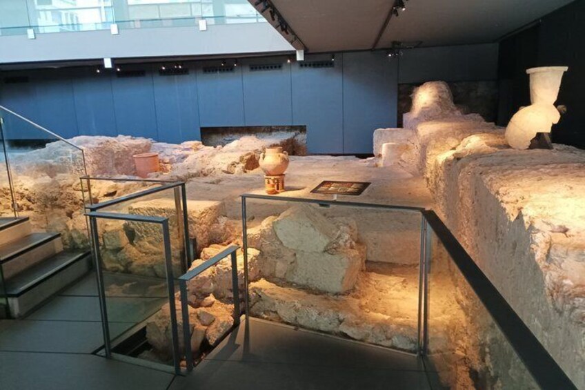 Een overdekte archeologische tentoonstelling met stenen constructies en een glazen balustrade. 5