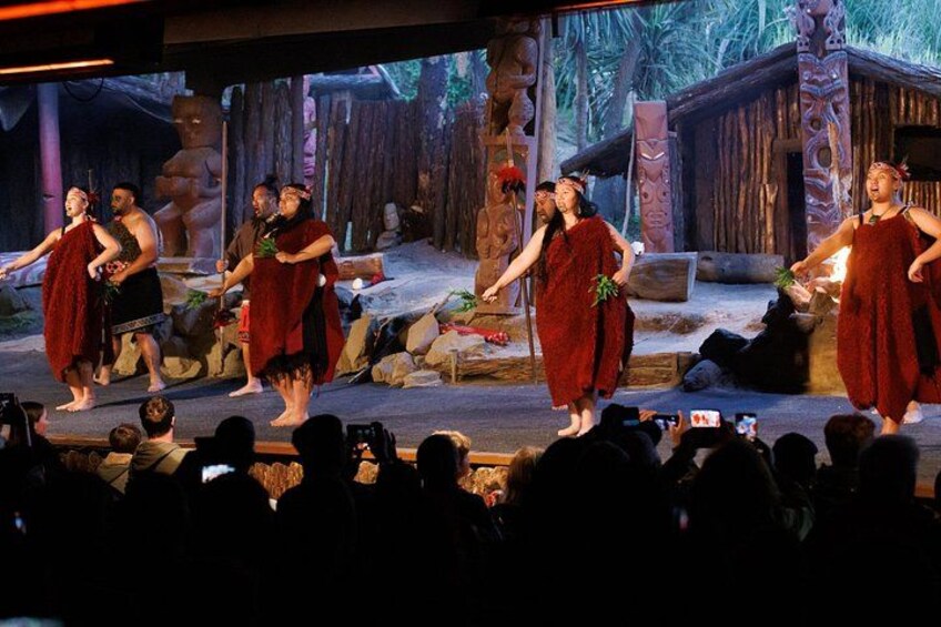 A stage with performers in red costumes, a wooden backdrop, and an audience. 1